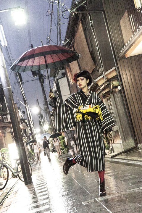 夜の細い路地。傘をさした和装のスタッフが歩いている