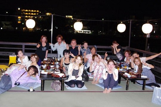 夜の座敷。長机を囲んで大勢が手をあげている