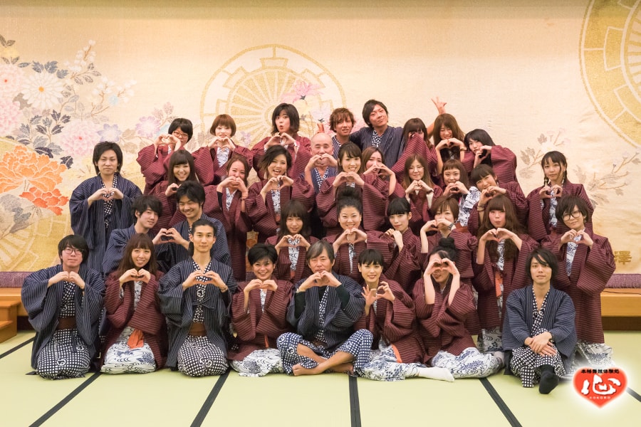 広間に全員が座り、指でハートをつくっている