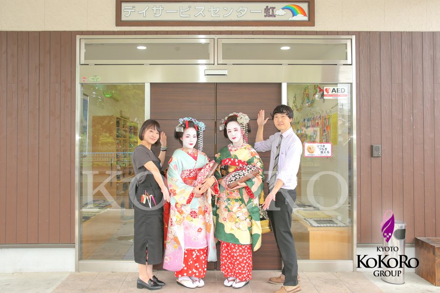 店の前で、舞妓姿の二人とスタッフが並んでいる
