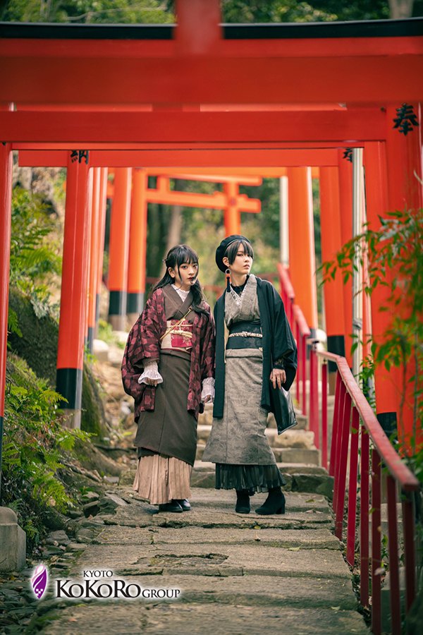 紅い鳥居の続く道に、着物の三人が立っている