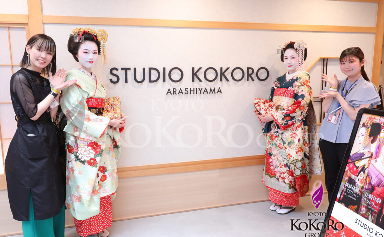 STUDIO KOKORO ARASHIYAMA の看板の前で、舞妓姿の二人とスタッフ