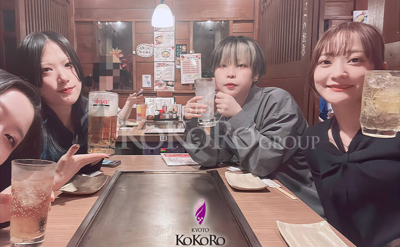 店の座敷で、四人が飲みものを手にしている